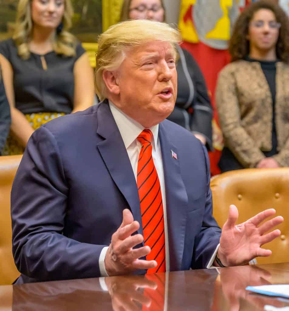 Donald Trump em uma mesa falando e gesticulando