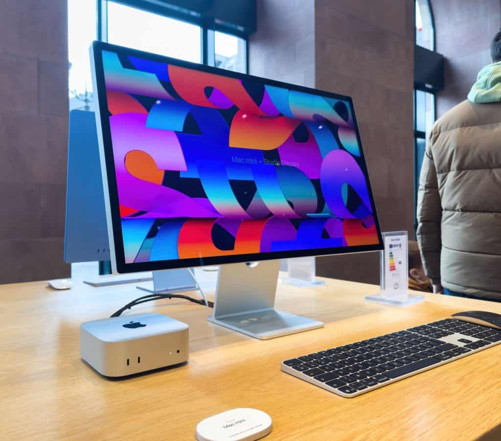 O Mac Mini é emparelhado com o Studio Display, Magic Keyboard e Magic Mouse, exibido em uma mesa de madeira em uma Apple Store