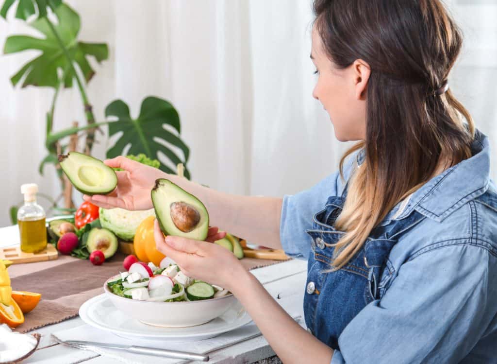 mulher segurando abacate com varias frutas na mesa