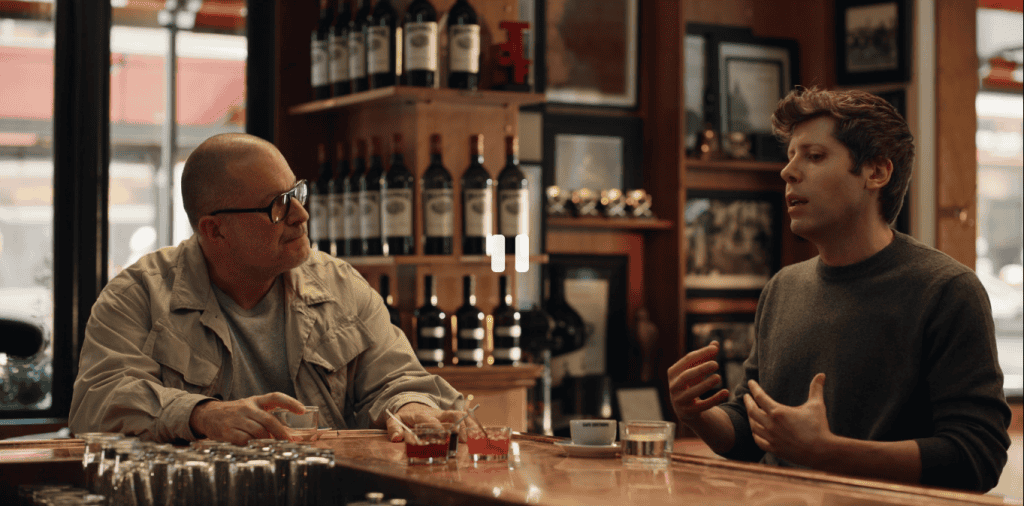 Imagem mostra o designer Jony Ive e o CEo da OpenAI, Sam Altman, conversando em um balcão de bar