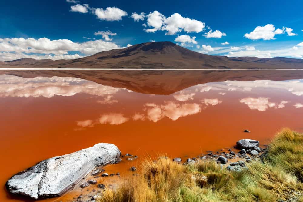 imagem mostra um rio da cor marrom clara com montanhas ao fundo