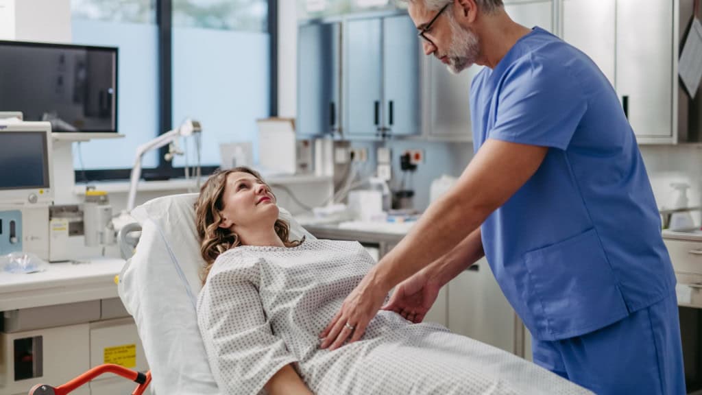 Médico palpando o abdômen da mulher, usando as mãos e pressão firme.