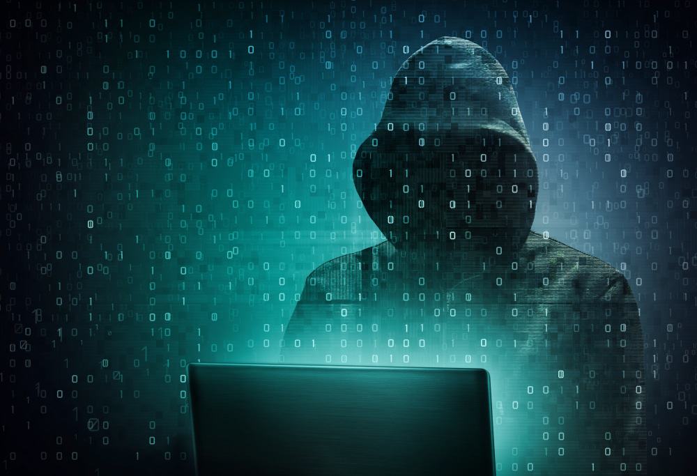 Hacker com capuz em frente ao computador e dados representando informações sobre toda a tela na tonalidade verde