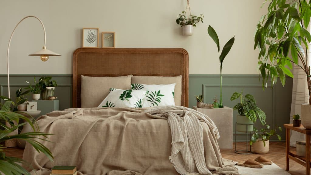 nterior de quarto quente e acolhedor com moldura de pôster simulada, cama boho, roupa de cama bege, parede verde com estuque, livros, chinelos marrons, plantas em vasos e acessórios pessoais. Decoração de casa. Modelo.