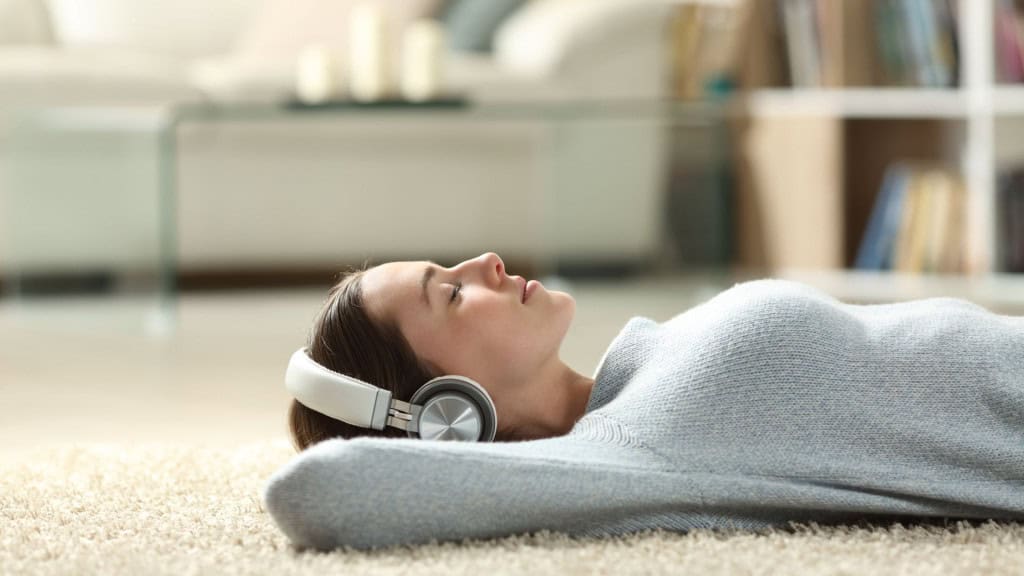 Retrato de vista lateral de uma mulher relaxada ouvindo música com fones de ouvido deitada em um tapete em casa