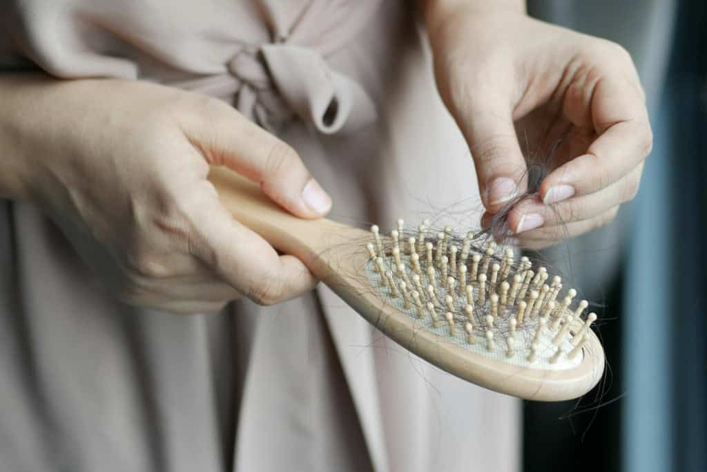 Mulher segurando escova de cabelo com um tufo de fios