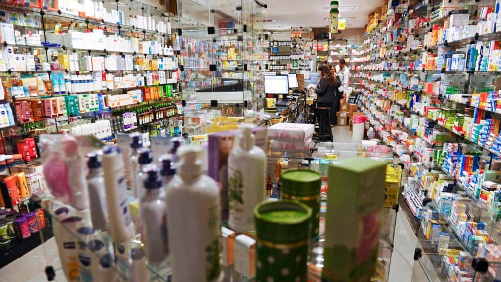 Pessoa ao fundo de uma farmácia abarrotada de remédios e outros tipos de produto