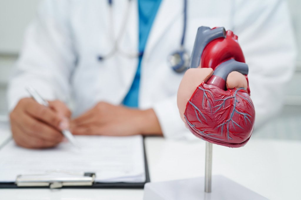 Médico cardiologista com modelo de coração em mesa de clínica