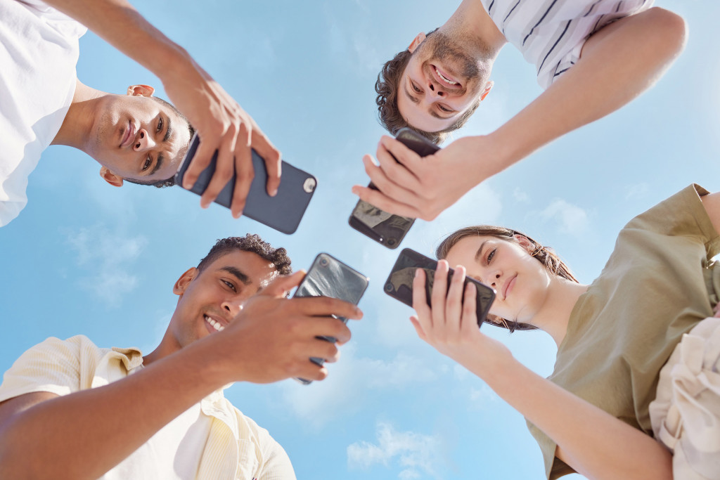 Quatro garotos sendo vistos de baixo com celulares em suas mãos