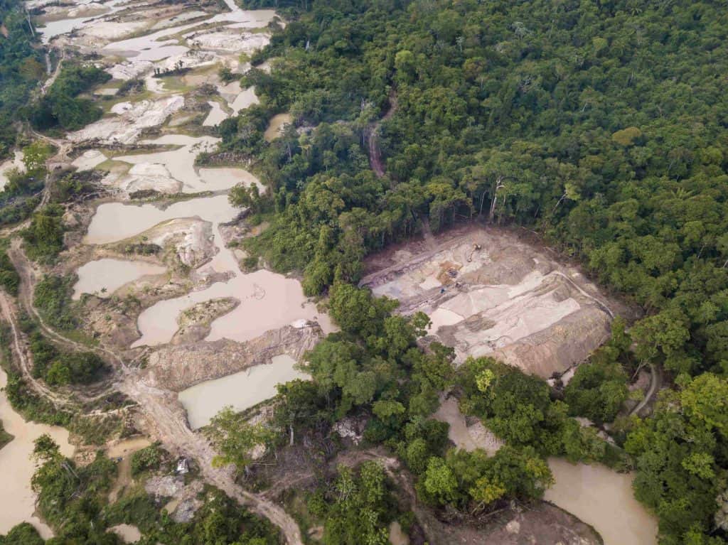 Aérea de garimpo ilegal na Amazônia revela desmatamento intenso, solo exposto e rio contaminado por mercúrio. A presença de tratores e estradas improvisadas evidencia a atividade predatória na região.