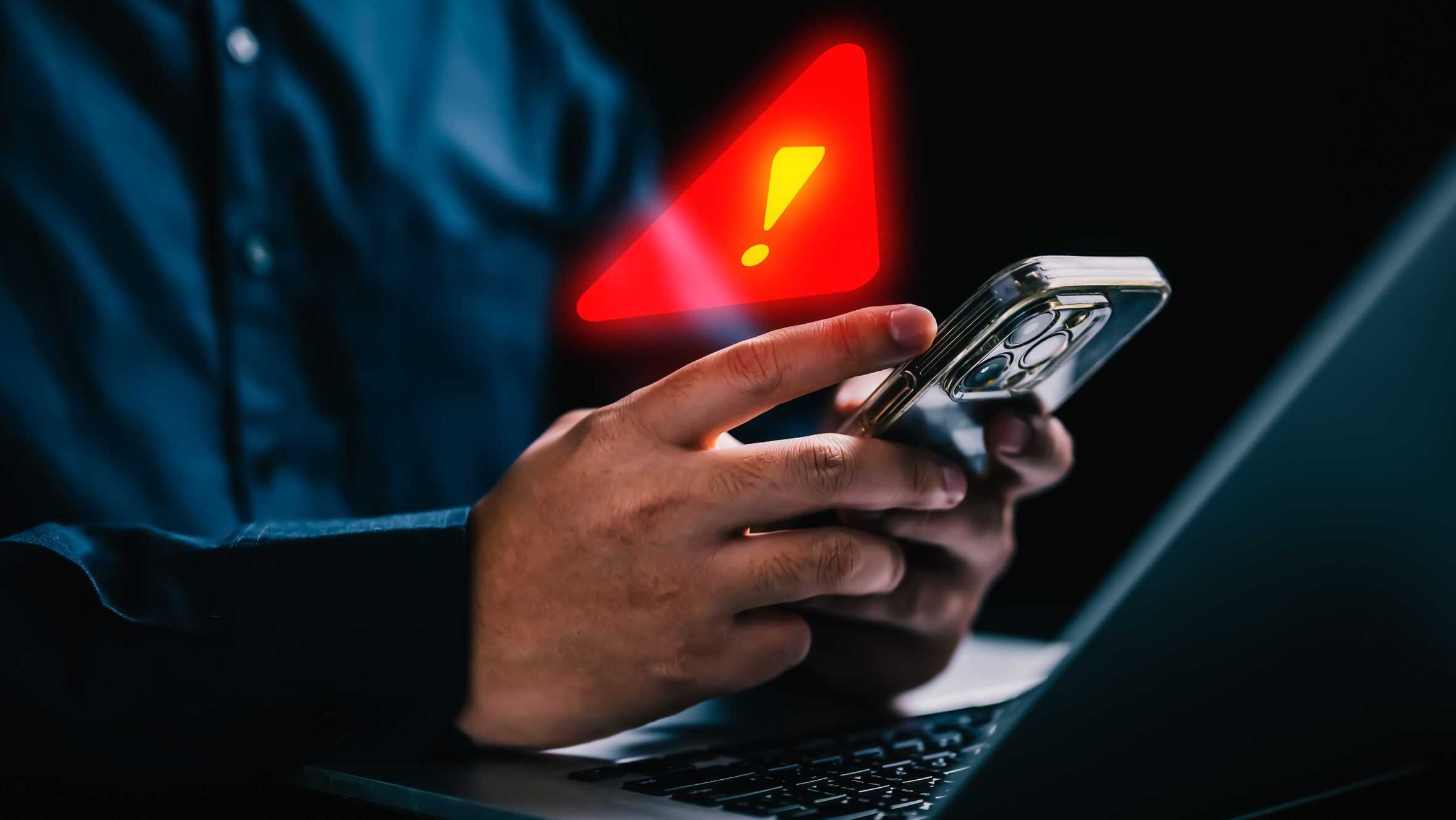 Símbolo de alerta acima de um celular que está sendo usado