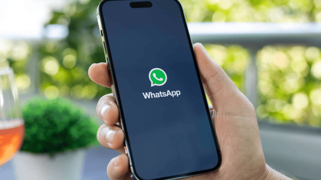 Pessoa segurando iPhone que está abrindo WhatsApp e exibe logomarca do aplicativo na tela