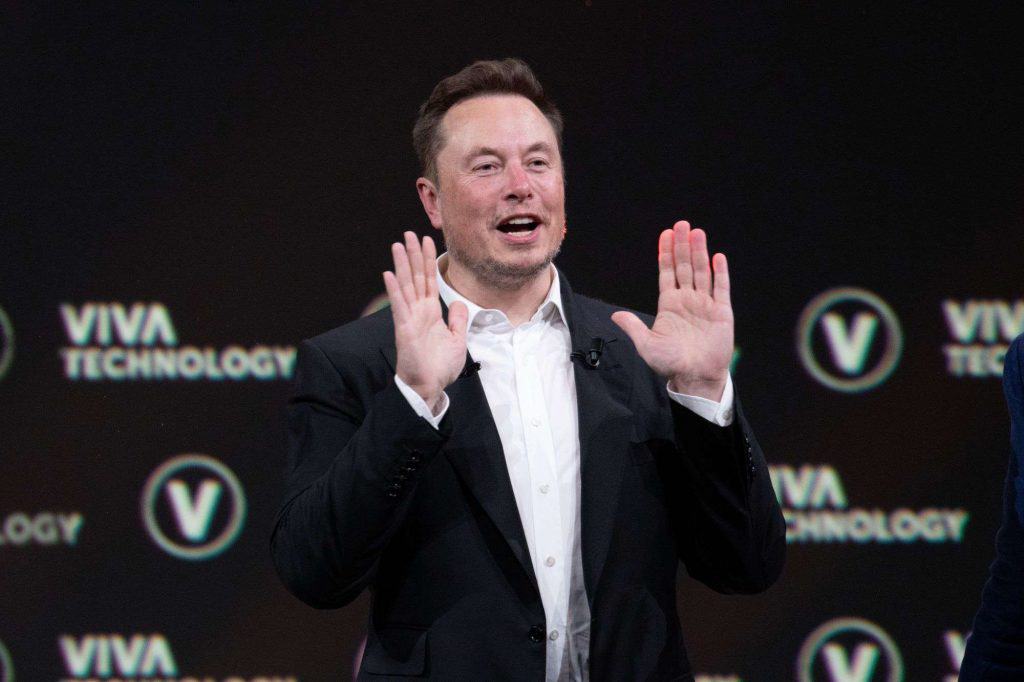 Elon Musk com a boca aberta e as mãos espalmadas