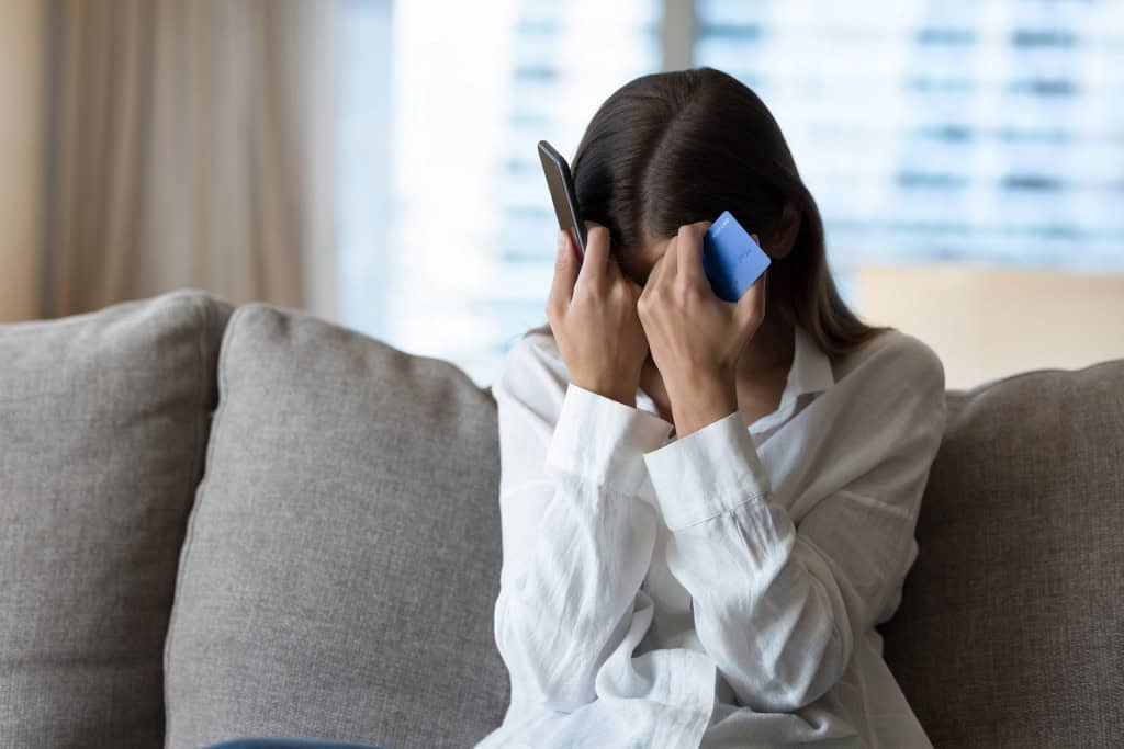 Mulher com as mãos no rosto e segurando um smartphone e um cartão de crédito