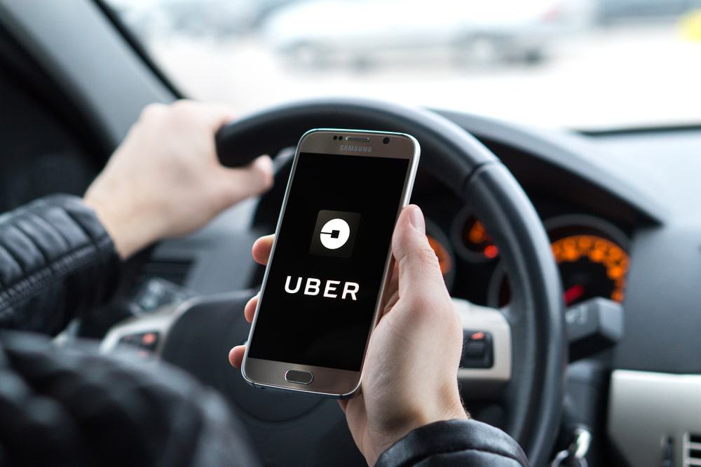 Uber driver holding smartphone in car.