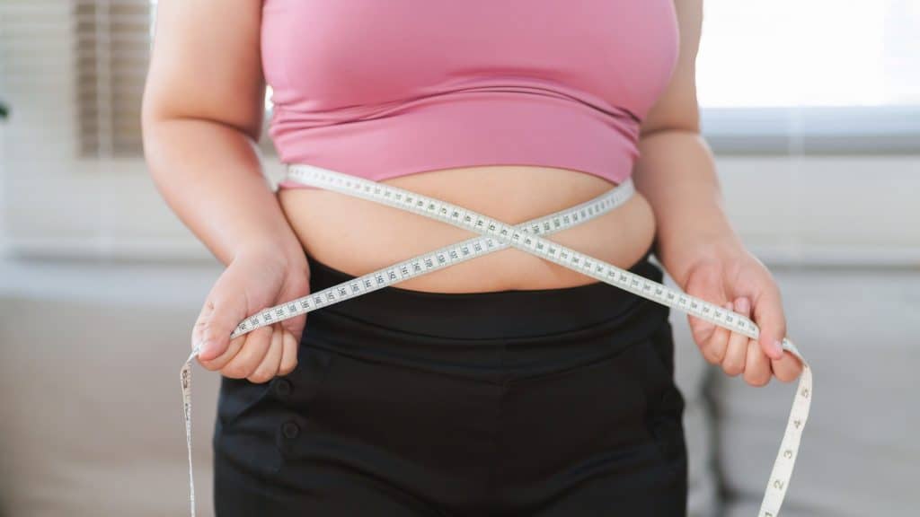 Mulher com sobrepeso mede sua cintura com fita métrica