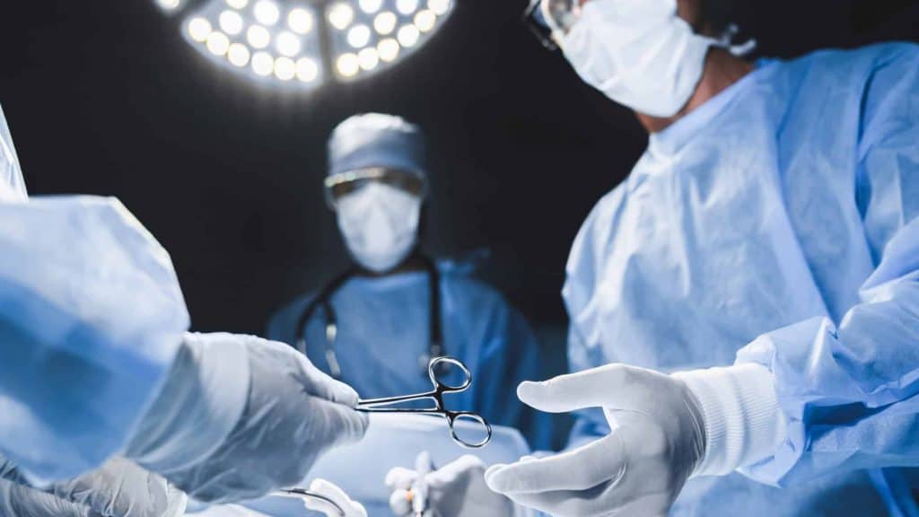 Médicos cirurgiões durante uma cirurgia passando instrumentos com uma luz vinda de cima