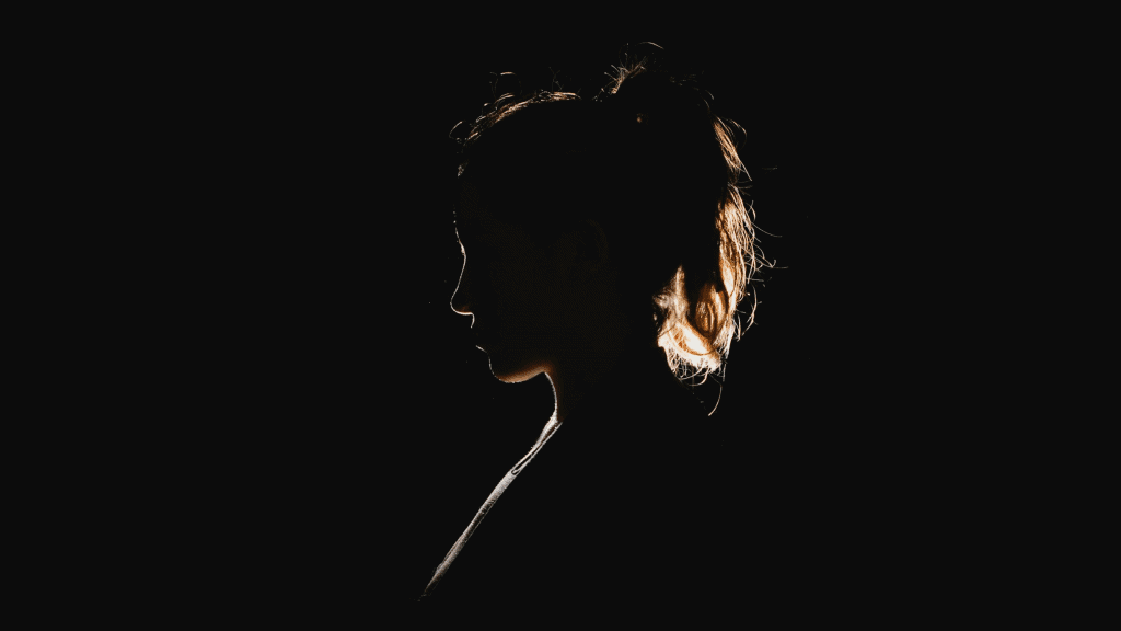 imagem mostra a silhueta mal iluminada de uma mulher em um ambiente completamente escuro