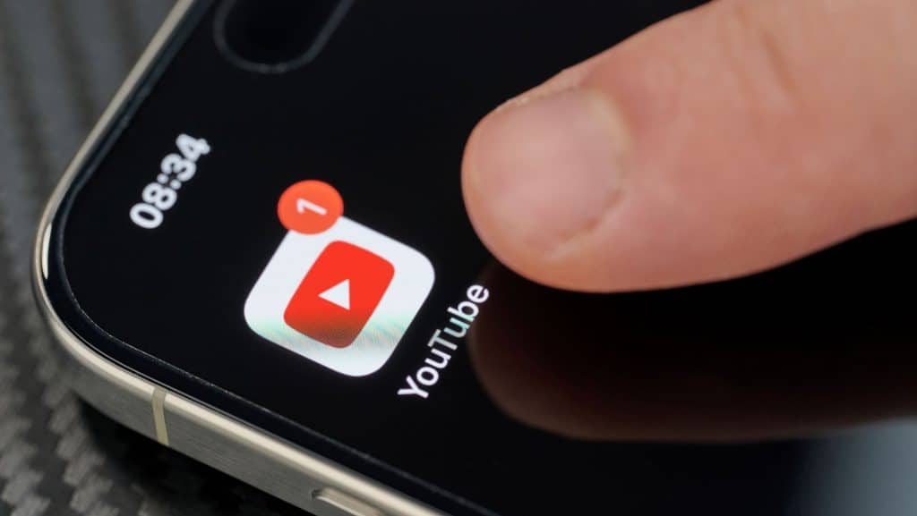 Pessoa com dedo sobre ícone do aplicativo do YouTube na tela inicial de um iPhone