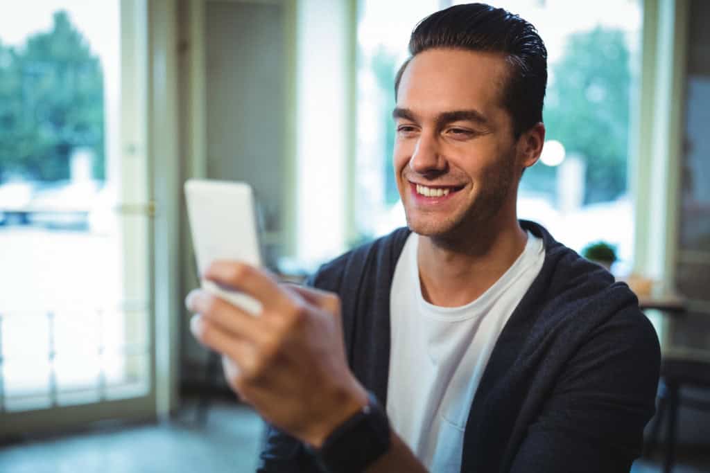 Homem segura o celular enquanto olha a tela e sorri