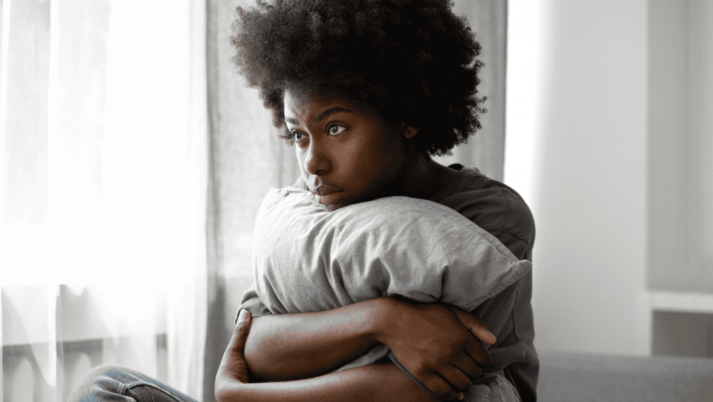 Mulher negra com semblante triste agarrada a um travesseiro.