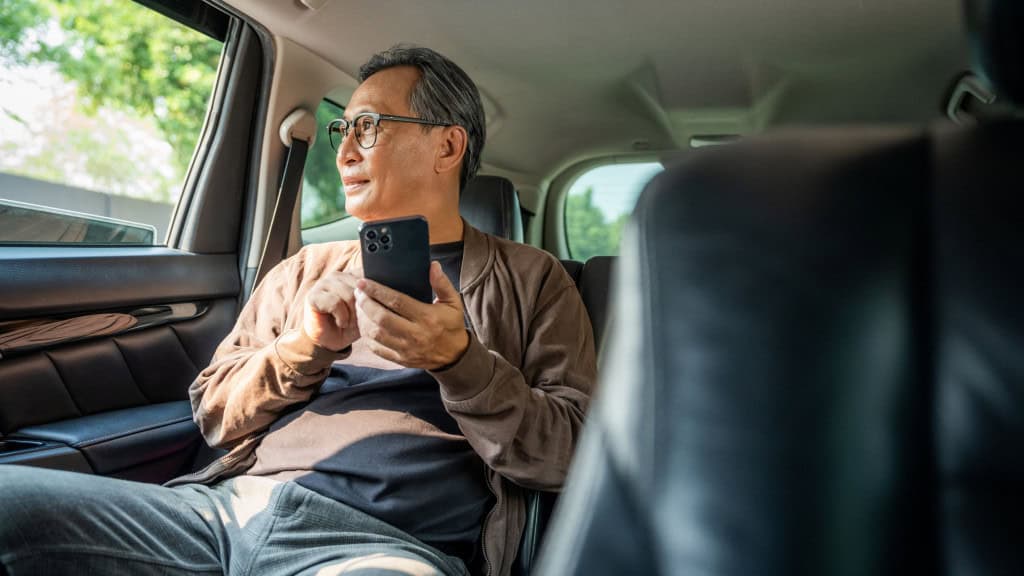 Japonês idoso no banco de trás de um carro segurando iPhone