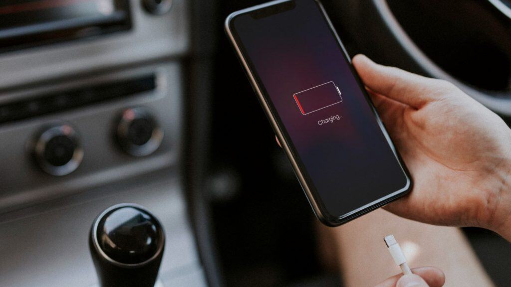 pessoa segura celular descarregado diante do painel do carro,com cabo para recarregar