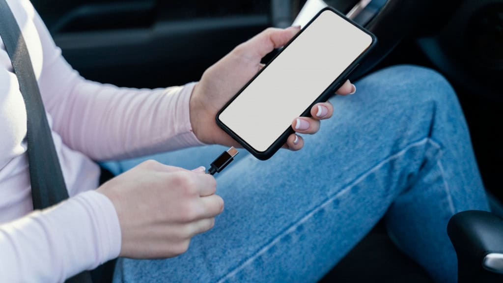 Mulher segura celular antes de plugar cabo no aparelho, dentro do carro