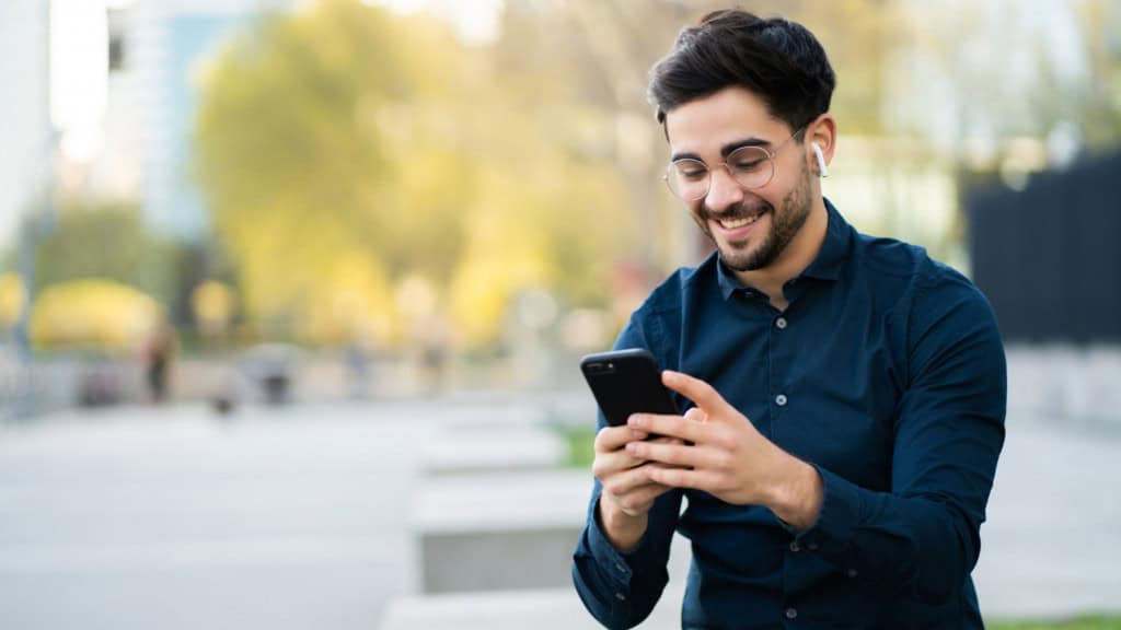 rapaz de óculos sorri e mexe no celular