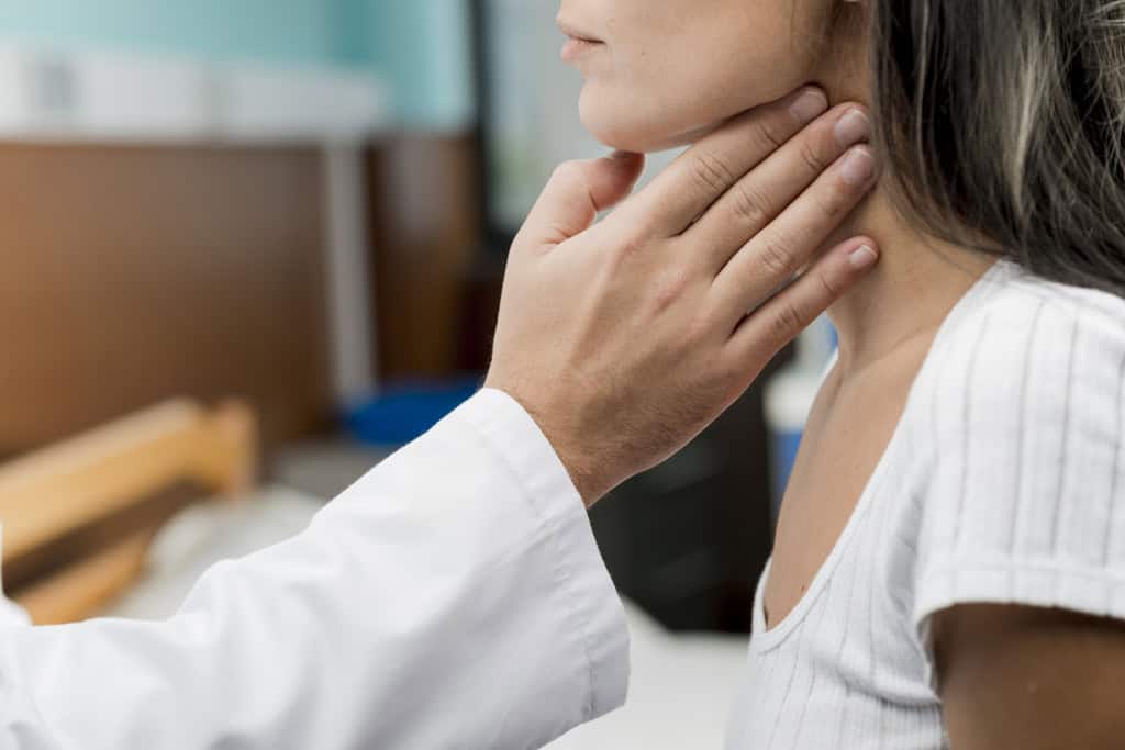 médico tocando a garganta de uma moça na região das amígdalas