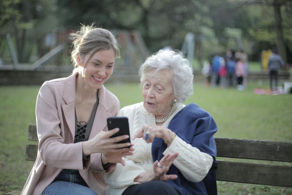 Golpes contra idosos, foto ilustrativa de mulher mais jovem mostrando celular para idosa