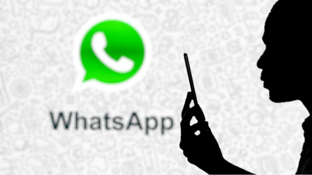 Silhueta de homem usando smartphone com ícone do WhatsApp messenger em segundo plano desfocado.