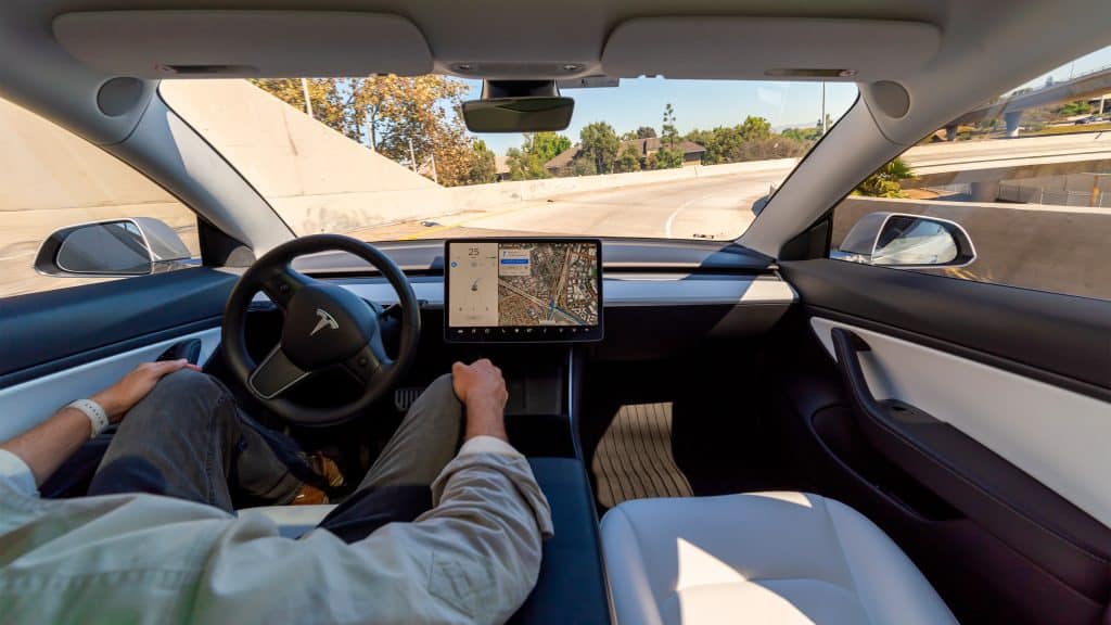 Homem com as mãos no colo andando em Tesla com Autopilot ligado