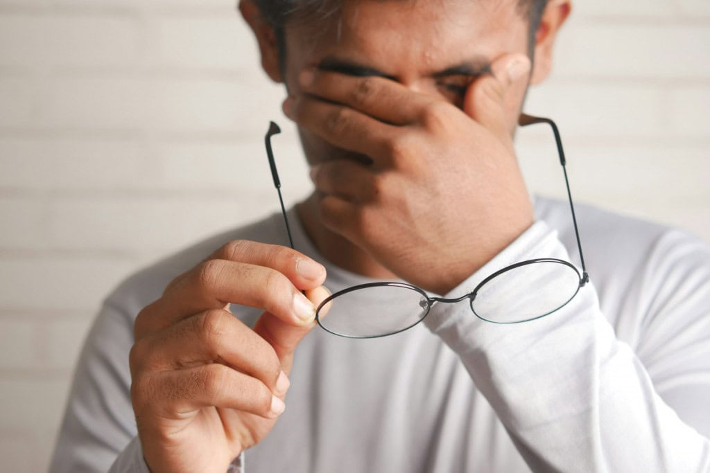 Homem esfregando olhos e segurando óculos em frente ao rosto