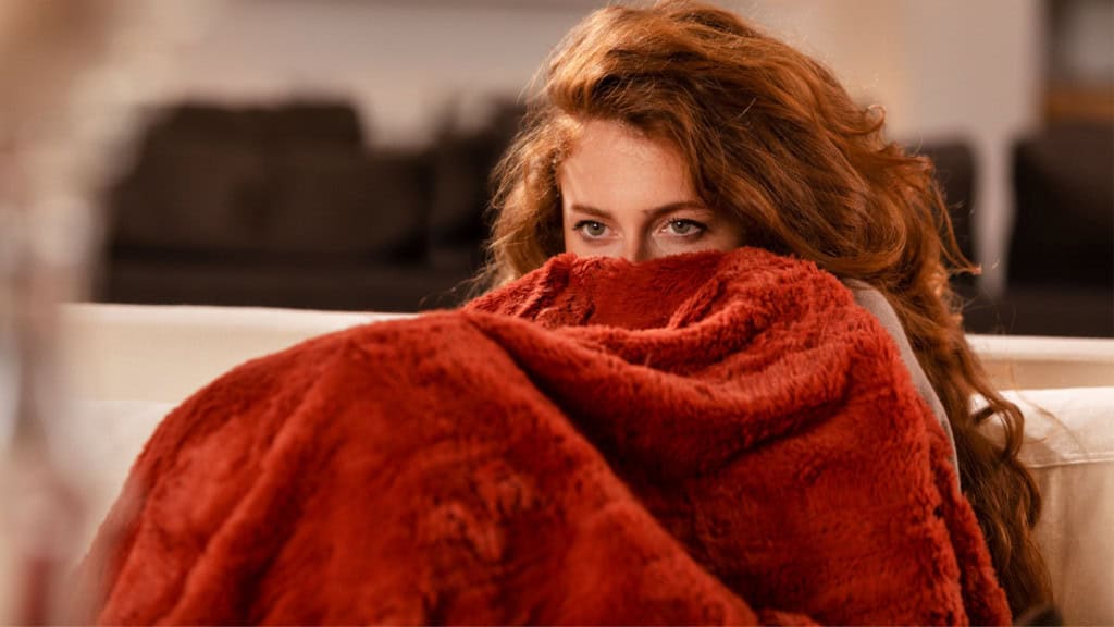 Mulher ruiva se protege com cobertor deixando apenas os olhos de fora