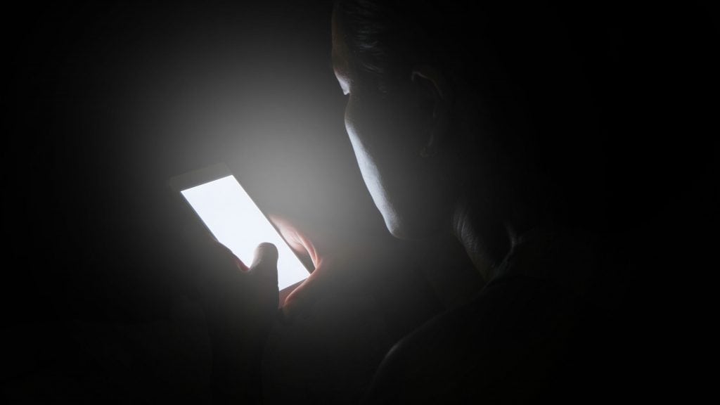 Mulher estressada usa o smartphone no escuro à noite, sem conseguir dormir. / Crédito: Me dia (Shutterstock)
