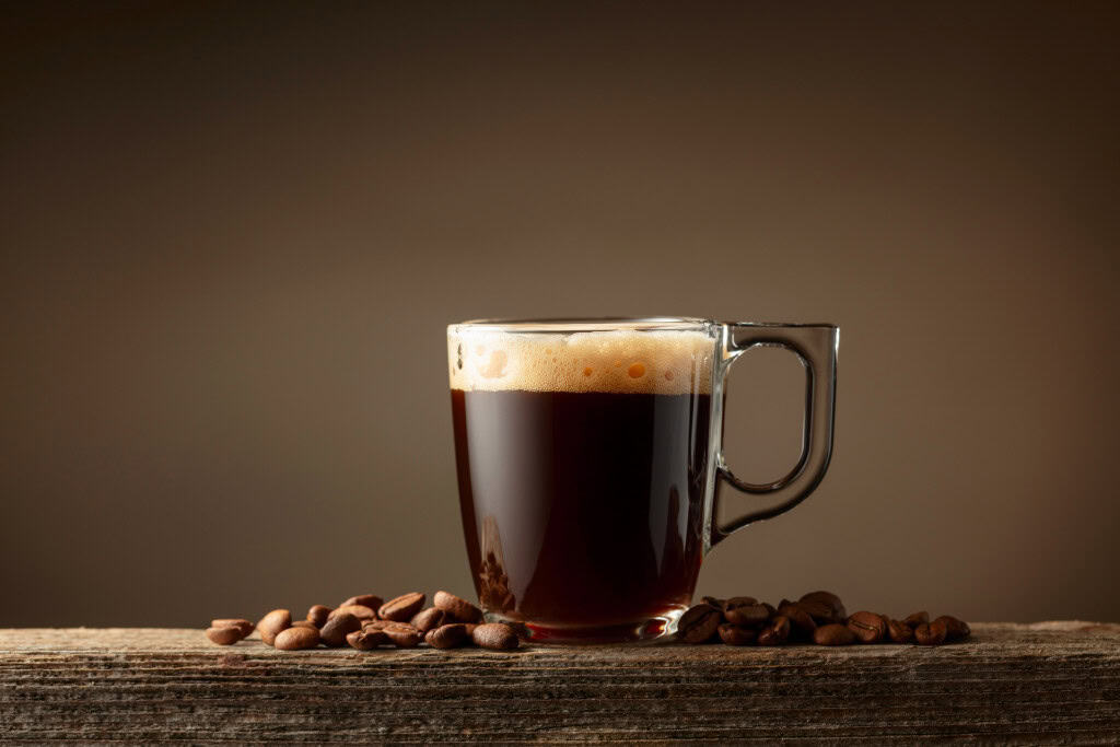 xícara de café no centro da imagem sobre uma superfície de madeira e grãos de café me volta
