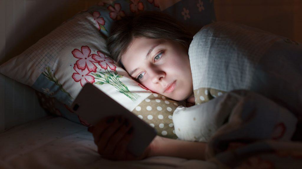 Garota cansada usando o celular na cama durante a madrugada.. / Crédito: Denis Mamin (Shutterstock/reprodução)