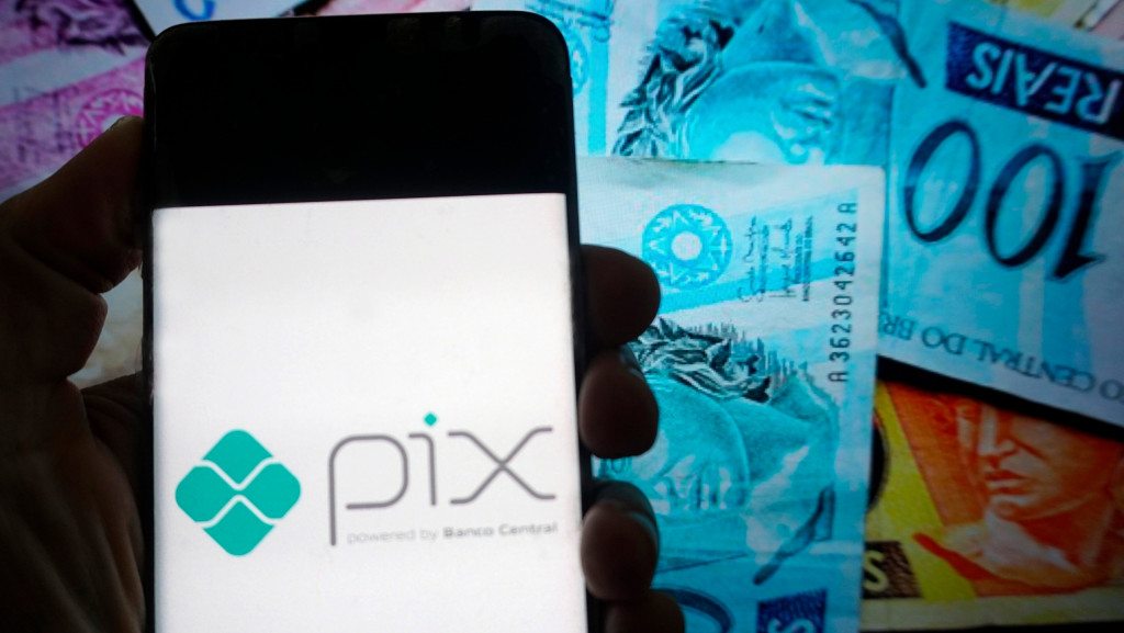 Ao fundo, notas de real; à frente, o logotipo do Pix em um smartphone