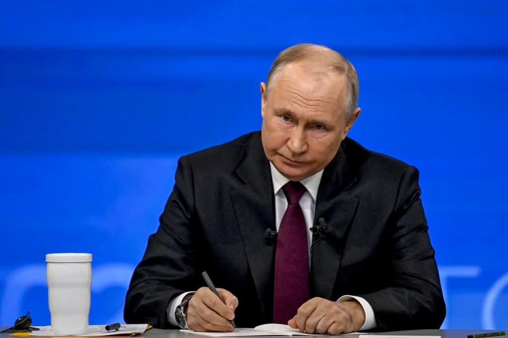 Vladimir Putin assinando um documento e olhando para frente