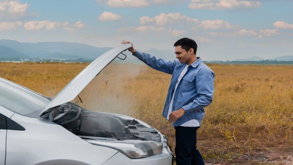 Carro superaquece e motor quebra com radiador com vazamento, vapor e fumaça de óleo quente saindo debaixo do capô. Jovem asiático motorista de carro em pé com o capô do carro aberto ao ar livre. Conceito de problema no motor do automóvel.