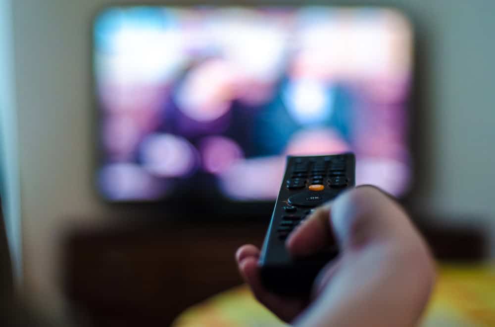 imagem mostra uma pessoa apontando um controle remoto para uma televisão