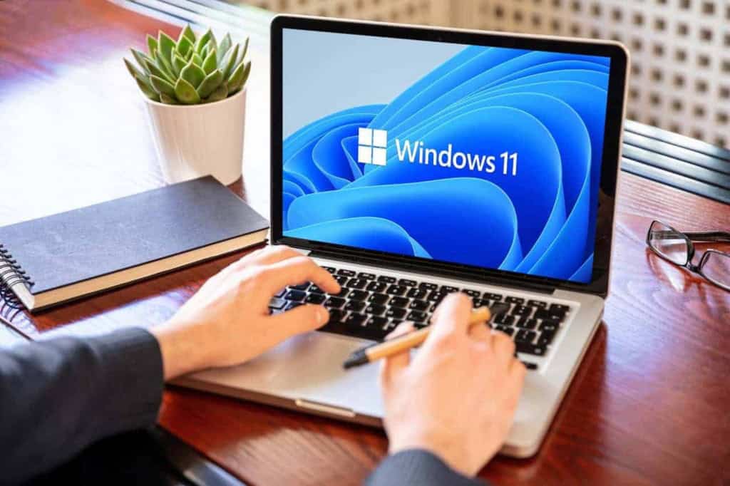 Homem utilizando um notebook com Windows 11 em uma mesa de madeira