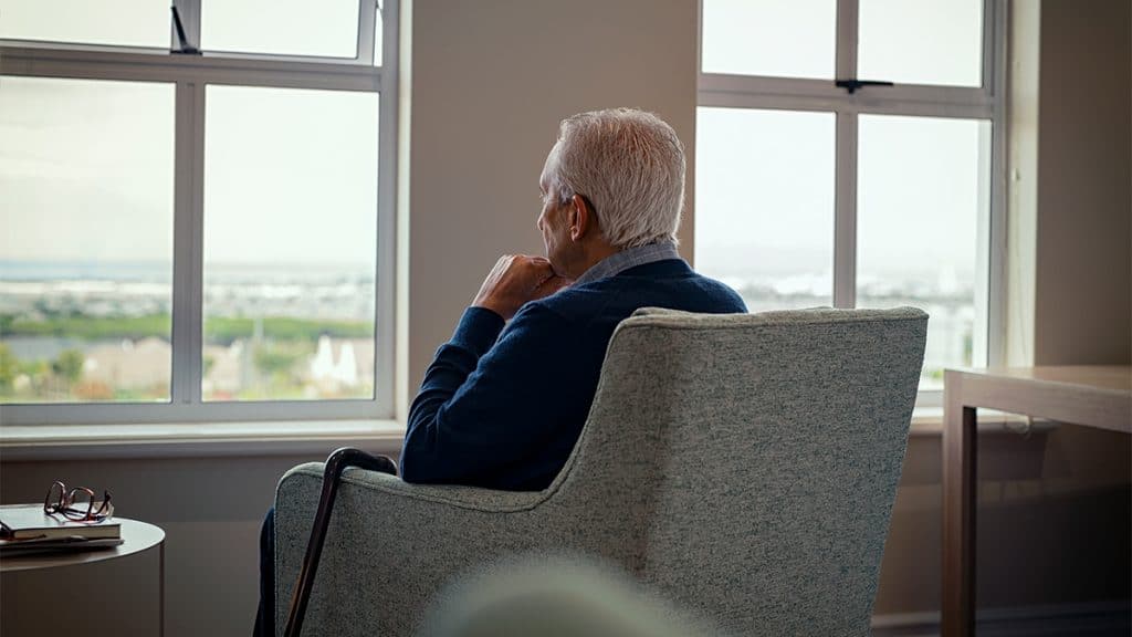 Idoso com Alzheimer sentado em poltrona olhando para janela