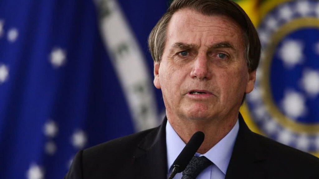 Ex-presidente Jair Bolsonaro falando em microfone na frente de uma bandeira do Brasil