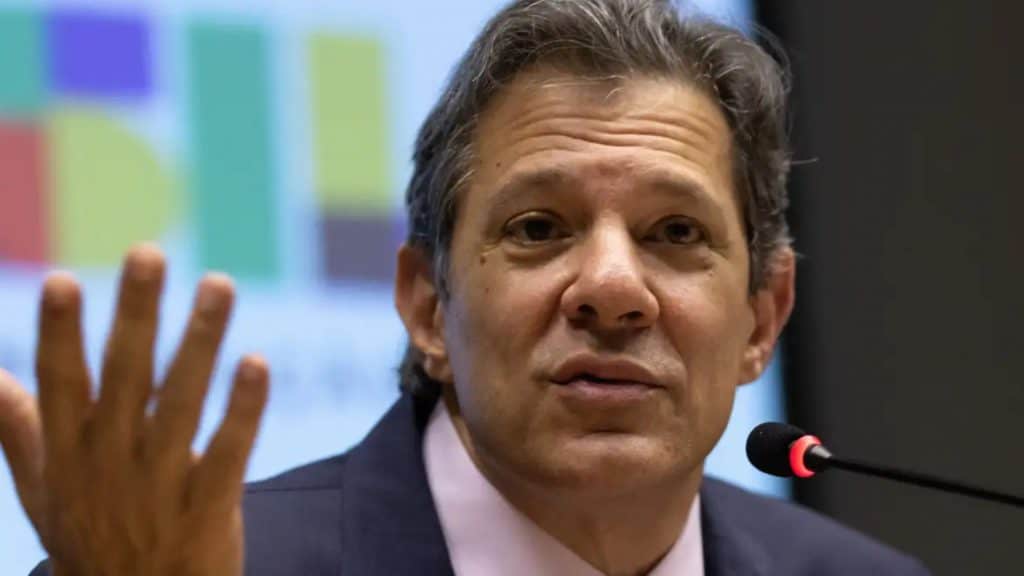 Ministro da Fazenda, Fernando Haddad, falando em microfone pequeno enquanto gesticula para cima com a mão direita