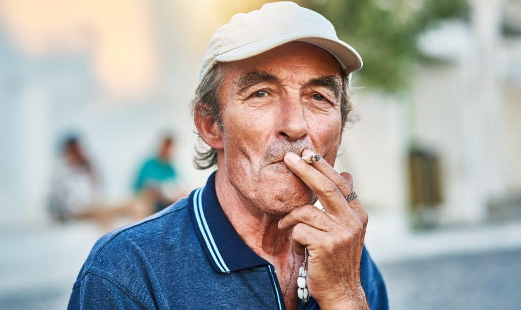 Homem idoso de boné em closeup fumando cigarro