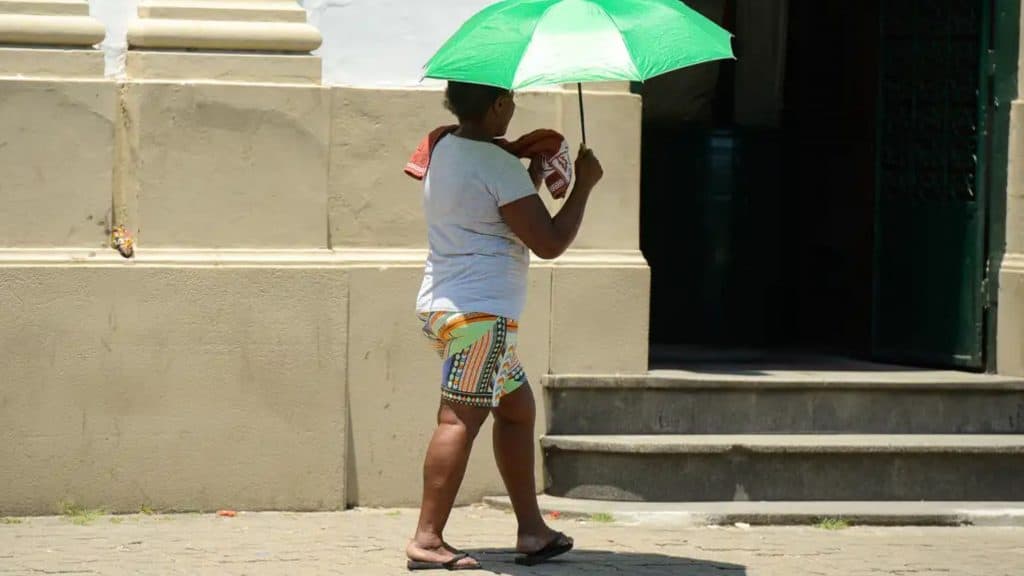 Mulher andando debaixo de sombrinha em dia quente