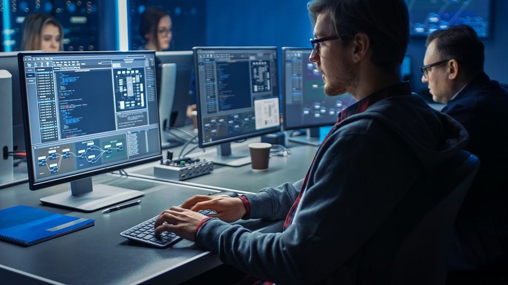 Imagem mostra homem sentado em uma mesa, digitando em um teclado de computador olhando para a tela do PC