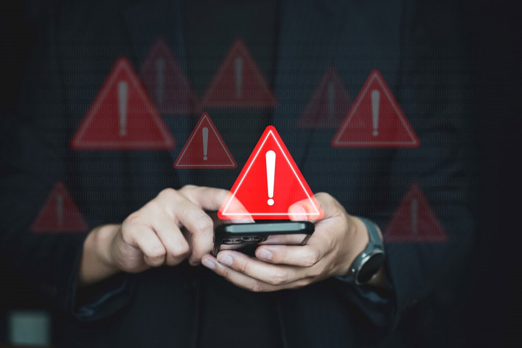 Vários sinais de alerta pairando em cima de um smartphone que está na mão de uma pessoa
